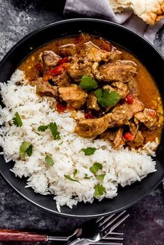 a bowl filled with rice and meat on top of a black plate next to silverware