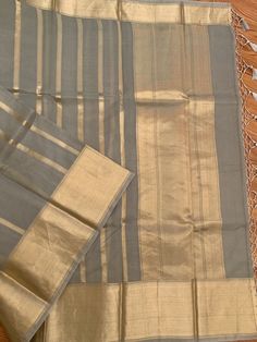 A very unique and stylish pure silk organza benarasi in a gorgeous gray shade with horizontal gold stripes. This is a very different benarasi, especially if you are looking to take a break from traditional sarees. The soft gold and gray look stunning together. The horizontal stripes give a modern look to the six yards. The fabric is extremely good quality silk organza. Saree is Silk Mark Certified. What is Kora Silk? Kora silk is untreated or un-dyed silk primarily made out of twisting only silk Transitional Gold Cotton Silk Dupatta, Gold Saree For Formal Eid Occasion, Elegant Gray Festive Traditional Wear, Elegant Chanderi Dupatta With Kora Details, Elegant Chanderi Dupatta With Kora, Gray Traditional Wear For Wedding And Festivals, Elegant Dupatta With Kora In Traditional Drape, Elegant Kora Dupatta In Traditional Drape, Gray Chanderi Traditional Wear For Festive Occasions