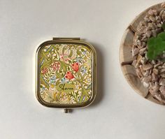 there is a small tin with flowers on it next to a bowl of rocks and a plant