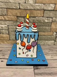 a birthday cake with candles and balloons on a blue tablecloth in front of a brick wall