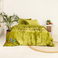 a bed with green sheets and pillows in a room next to a potted plant