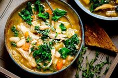 a bowl of chicken and white bean soup on a wooden table next to some bread