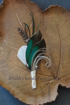 a green and black feather on a leaf with some white adhesivement around it