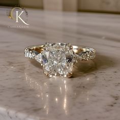 an oval cut diamond ring with side stones on a marble countertop in a hotel room