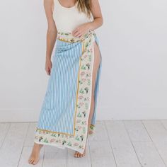 a woman in a white tank top and blue floral print skirt standing on the floor