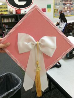 a pink and white graduation cap with a tasseled bow at the top, sitting on a desk