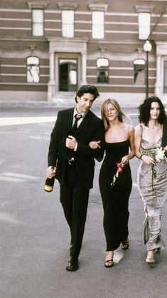 three people are walking down the street in formal attire and one is holding a flower