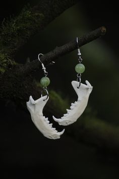 two white earrings with green beads hanging on a tree branch in front of a dark background