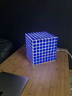 a blue cube lamp sitting on top of a wooden table next to a laptop computer