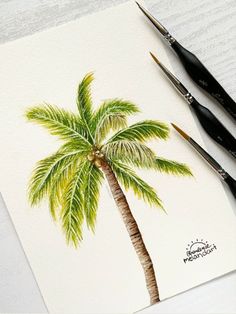 two paintbrushes sitting on top of a piece of paper with a painting of a palm tree