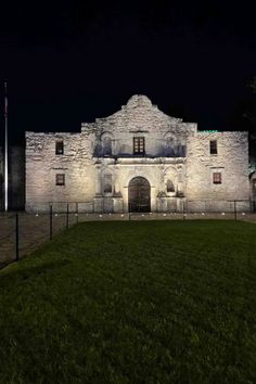 an old building lit up at night with the lights on and grass in front of it