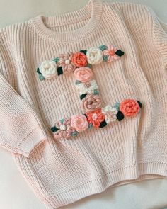 a pink sweater with flowers on it and the letter f spelled out in floral letters