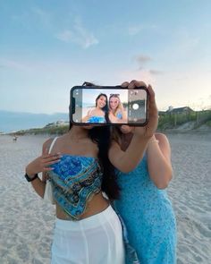 two women taking a selfie on the beach with their cell phone in front of them