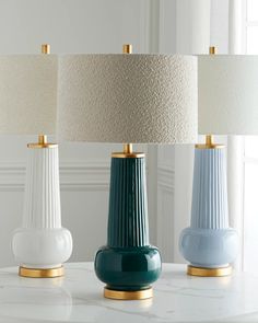 three different colored lamps sitting on top of a white table with gold trimmings