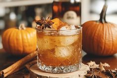 a glass filled with ice and cinnamon sitting on top of a table next to two pumpkins