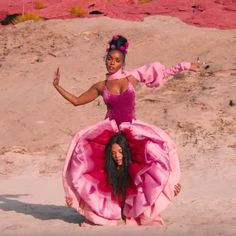 two girls in pink dresses standing on the sand with their arms out and one girl is holding her head