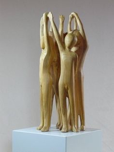 three wooden figures standing on top of a white pedestal with their arms in the air