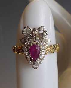 A FINE  9CT SOLID GOLD VICTORIAN STYLE BOW TOPPED HEART SHAPED SWEETHEART RING. THE CENTRE SET WITH A PEARSHAPE REAL RUBY AND SURROUNDED WITH  REAL ROUND CUT DIAMONDS AND ALSO DIAMONDS SET IN BOW.. SET ON A DECORATIVE SIDED SHANK. RING SIZE uK -N, USA- 6.75 , HAS FULL ENGLISH HALLMARKS FOR 9CT GOLD.. LOOKS VERY PRETTY WHEN WORN. Pear-shaped Brilliant Cut Yellow Gold Ruby Ring, Yellow Gold Heart Cut Ring With Rose Cut Diamonds, Antique Gold Ruby Ring With Brilliant Cut, Elegant Yellow Gold Ruby Ring With Heart Cut, Pear-shaped Gold Ruby Ring With Diamonds, Victorian Heart-shaped Anniversary Rings, Pear-shaped Ruby Diamond Ring In Gold, Classic Heart-shaped Ruby Ring For Formal Occasions, Classic Heart-shaped Ruby Ring