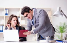 a man and woman in an office setting looking at a laptop