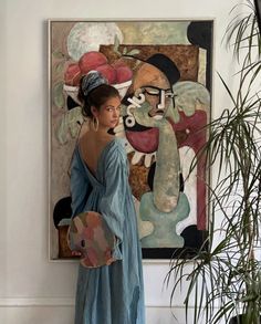 a woman is standing in front of a painting and holding a fan while wearing a blue dress