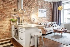 a living room filled with furniture and a brick wall behind the kitchen island in front of a window