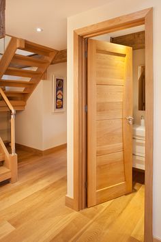 an open door leading to a bathroom and stairs in a room with hardwood floors, white walls and wood flooring