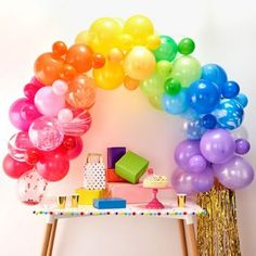 a table topped with lots of balloons next to a rainbow arch filled with confetti