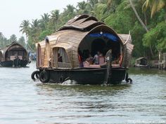 some people are riding on a boat in the water near palm trees and houses with thatched roofs