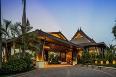 the entrance to a resort at dusk with palm trees in the foreground and lights on