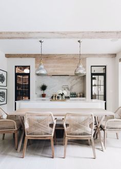 a dining room table with chairs and pictures on the wall behind it in front of an open kitchen