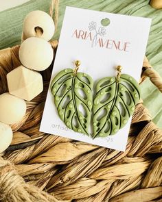 a pair of green leaf shaped earrings sitting on top of a basket next to eggs