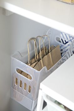 some bags are hanging from the wall in a kitchen closet with white cabinets and drawers