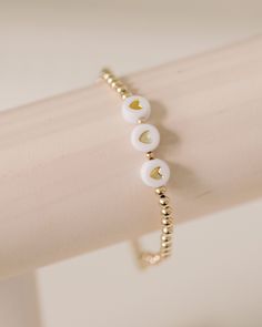 handcrafted stretch bracelet made with white + gold heart beads and 14k gold filled 3mm beads customize with 3-6 letters - name, monogram, city, anything you choose! made by artists in the USA Length - 6.5 inches Dainty White Adjustable Stretch Bracelet, Dainty White Round Beads Stretch Bracelet, Dainty White Stretch Bracelet For Everyday, Adjustable White Dainty Stretch Bracelet, White Adjustable Dainty Stretch Bracelet, Gold Heart-shaped Adjustable Stretch Bracelet, Gold Adjustable Heart Shaped Stretch Bracelet, Adjustable Gold Heart-shaped Stretch Bracelet, Adjustable White Name Bracelet With Gold Beads