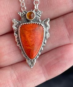 One-of-a-kind southwest inspired arrowhead pendant featuring ethically sourced coral and amber on patterned sterling silver.  This is a slightly smaller version of the arrowheads that I have available.  Perfect size and accent for everyday wear.  Arrowheads have deep cultural meaning for the native Americans and this design seeks to embody those beliefs and bestow its powers upon the wearer.   They believe that wearing an arrowhead pendant is a symbol of strength and protection. It is likewise k Handmade Sterling Silver Arrowhead Necklace, Unique Arrowhead Jewelry With Natural Stones, Unique Arrowhead Natural Stone Jewelry, Unique Orange Sterling Silver Necklace, Southwestern Arrowhead Jewelry Gift, Southwestern Style Arrowhead Jewelry Gift, Unique Orange Sterling Silver Jewelry, Arrowhead Pendant, Symbol Of Strength