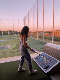 a woman standing on top of a grass covered field next to a fence and holding an electronic device