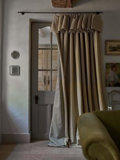 a living room with a green chair and striped curtains hanging on the wall next to an open door