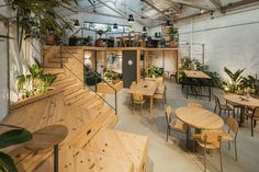 an indoor cafe with wooden tables and chairs, plants on the wall and stairs leading up to the second floor