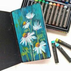 an art journal with crayons and pastels next to it on a table