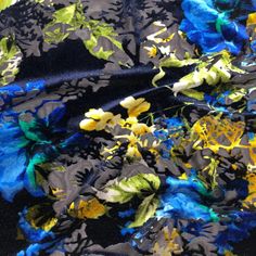 blue and yellow flowers on black fabric with green leaves in the center, closeup