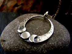 A Silver triple moon circle necklace with a hammered and oxidised background , The three little moons sit on the base of a silver crescent and are polished for a little bit of shine . Great for the moon lover !! The little moons stand out against the hammered and oxidised background. The pendant sits comfortably on a sterling silver 18 cable chain. If you would like a different chain , please just ask and I will try to accommodate you  This is a great everyday pendant , but would look also stunning with a simple black dress The polished finish catches the light and the design is simple and elegant. The pendant is a substantial 1  inches across and 1 and a bit  inches in height with bail. for more designs please visit www.etsy.com/shop/dagdesigns Thanks for looking! Jewelry Metalsmithing, Metal Jewelry Handmade, Gem Necklaces, Everyday Pendant, Silversmith Jewelry, Celestial Pendant, Hammered Pendant, Moon Circle, Galaxy Jewelry