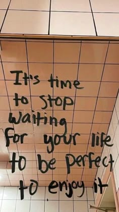 graffiti on the ceiling of a bathroom stall saying it's time to stop waiting for your life to be perfect to enjoy it