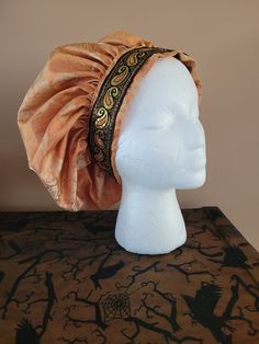 A renaissance staple!  Classic muffin cap style...  keep it plain to match all your outfits, or add some feather and button embellishments.    Cap is made from a soft orange and cream damask fabric and the band is trimmed with black, orange and gold jacquard trim.  All edges are finished, and there is no elastic in the band. Don't forget to check your head measurement! Standard shipping will ship Small Packets air mail, and take approx. 8 business days to arrive in Canada and the U.S.  Overseas Adjustable Costume Bonnet, Adjustable Costume Hats And Headpieces, Adjustable Costume Cap, Adjustable Costume Hat One Size, Adjustable Cap For Costume, Adjustable Gold Hat For Costume Party, Gold Adjustable Hat For Costume Party, Adjustable Ceremonial Costume Hat With Curved Brim, Adjustable Ceremonial Cap Costume Hat