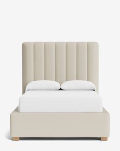 an upholstered bed with white sheets and pillows