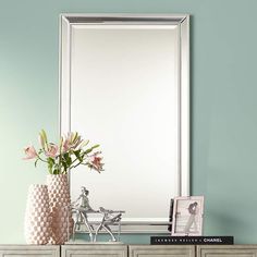 a vase with flowers sitting on top of a dresser next to a mirror and photo frame