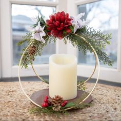 a white candle sitting on top of a table next to a christmas wreath with flowers