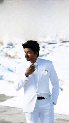 a man in a white tuxedo poses for the camera with his hand on his chest