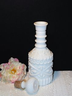 a white vase sitting on top of a table next to a bottle and a flower