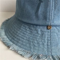 a light blue hat with fringes on the brim and side panel, sitting on top of a white surface