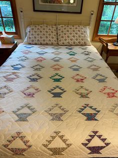 a bed with a quilt on top of it next to two nightstands and windows