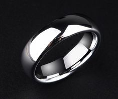 a white gold wedding ring on a black surface with the light reflecting off it's side